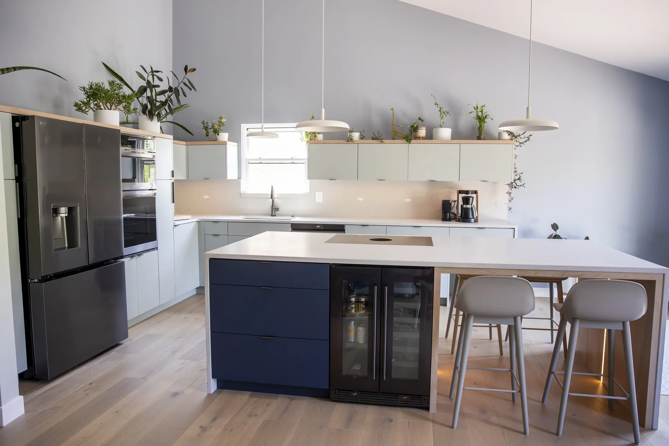 Wide kitchen with navy island, sage green cabinets, oak shelf with plants and pendant lights