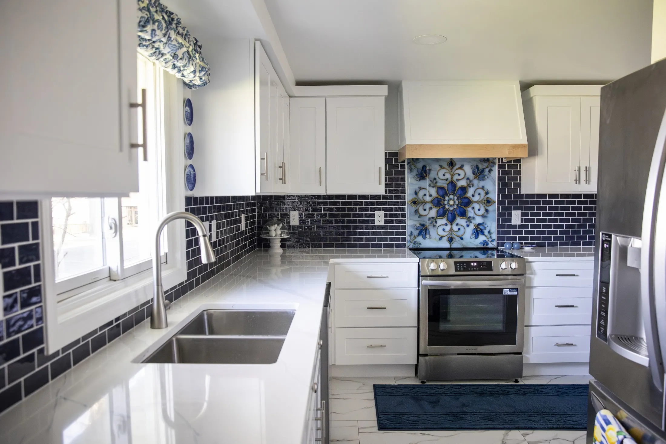 White shaker kitchen with navy subway tile, floral tile panel and wood-banded hood