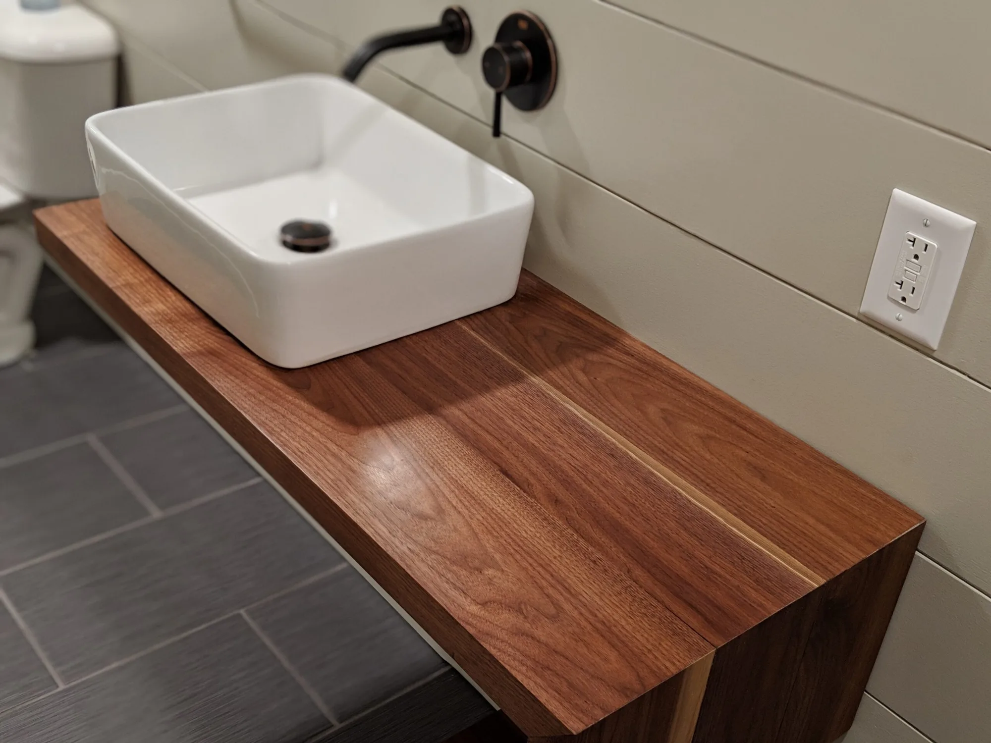 Walnut waterfall vanity with a white vessel sink and black wall faucet